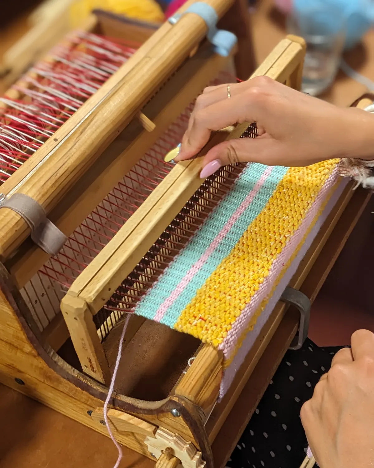 Tissage à rayures jaunes, turquoise et roses sur un petit métier à tisser en bois pendant un stage
