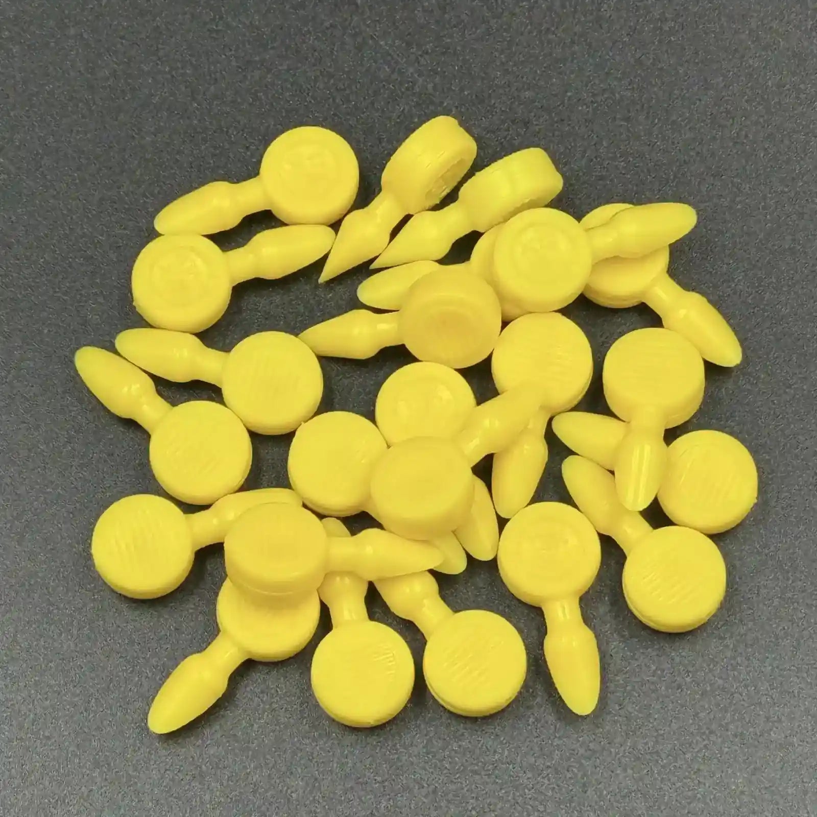 Texsolv Pfeilstecker in Gelb – Kunststoffstecker zur Fixierung von Texsolv Ösenschnur, rundes Design, auf dunkler Oberfläche lose angeordnet